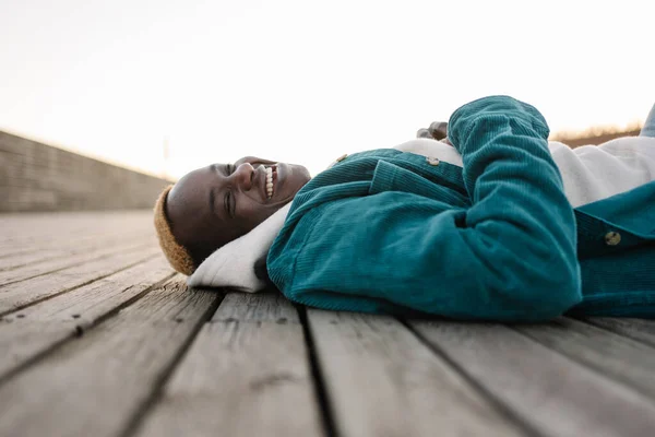 Lykkelig, svart, afroamerikansk mann som ligger på tregulvet og ler med positive følelser – stockfoto