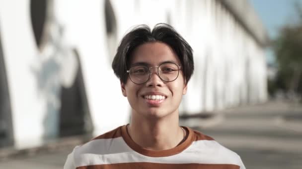 Gözlüklü, gülümseyen ve olumlu duygularla kameraya bakan mutlu Asyalı genç erkek öğrencinin portresi başarılı bir yaşam tarzının keyfini çıkarıyor. — Stok video