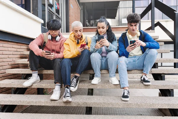 Monikulttuurinen ryhmä nuoria ystäviä matkapuhelimia ja sosiaalisen median - Opiskelijat istuu yliopiston kampuksella kirjoittamalla älypuhelimilla — kuvapankkivalokuva