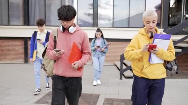 Üniversite öğrencileri kolej okulunda akıllı cep telefonları kullanarak yürüyorlar - Sosyal medya ve Sanal İnternet Ağ Bağımlılığı — Stok video