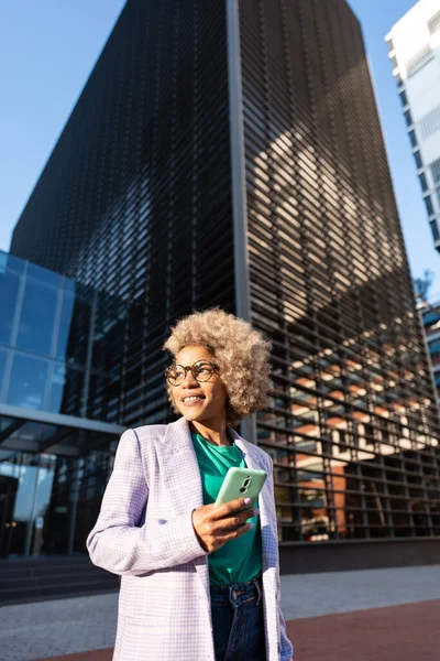 Modern cheerful african american executive business woman outside the workspace office, holding a smartphone — kuvapankkivalokuva