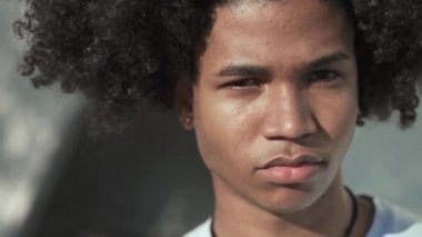 Afro saçlı, ciddi görünüşlü, gülümseyen ve kameraya kendinden emin genç Afrikalı Amerikalı adamın yakın portresi.