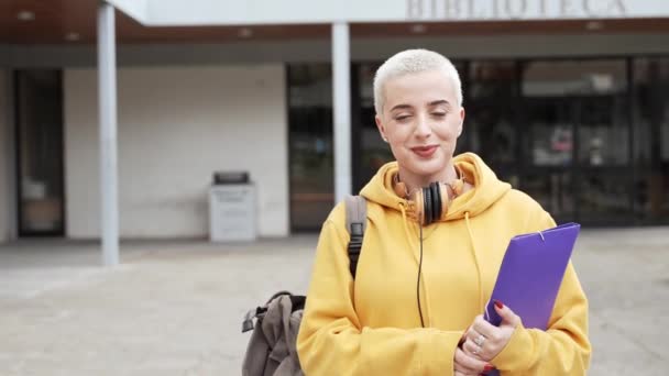 Étudiante universitaire blonde aux cheveux courts rasés Souriant regardant le dossier de la caméra à l'extérieur du bâtiment de l'Université — Video