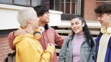 Üniversite öğrencilerinden oluşan bir grup arkadaş üniversite binasının dışında konuşarak ve gülerek iyi vakit geçiriyorlar.