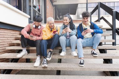 Mutlu arkadaşlar cep telefonu ve sosyal medya kullanıyor - üniversite kampüsünde oturan öğrenciler akıllı telefonlarda uygulama kullanıyorlar
