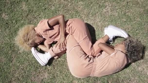 Afrikanska amerikanska systertvillingar som ligger på gräset och sover tillsammans i fosterställning. Känslomässig anknytning i familjen — Stockvideo