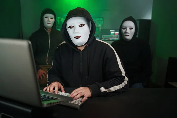 Team of Masked Hackers Using Computer to inflict Data Breach Attack on Government Servers. Anonymous Digital Crime
