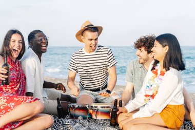 Genç arkadaşlar yaz tatillerinde plaj partisinde müzik çalıp bira içerek eğleniyorlar.