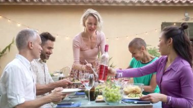 Arkadaşlara sağlıklı makarna salatası servis eden neşeli sarışın kadın akşam yemeği partisinde harika vakit geçiriyor. 