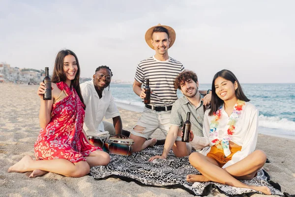 Group of multicultural friends sitting on the beach in summer music festival