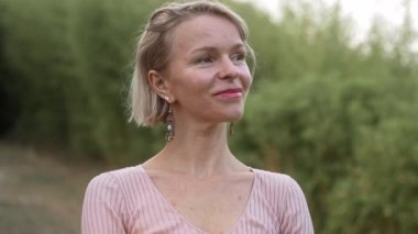 Sarışın kadın orman bahçesinde duruyor, temiz hava soluyor, alacakaranlıkta doğayı düşünüyor. Kadın, parkta sakin ve huzurlu bir hayatın tadını çıkarıyor.