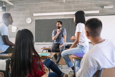 Genç öğrenciler lise eğitiminde dost canlısı genç erkek öğretmenler ile grup tartışmasını dinleyip sohbet ediyorlar