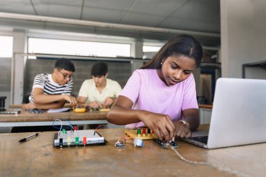 African American High School teenage Student programming electronics circuit board in the science technology workshop - Learning Digital Innovation in Education