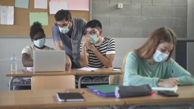 Teacher helping students learning at High school. Pupils wearing medical face masks working with laptop. Back to School in Covid Pandemic