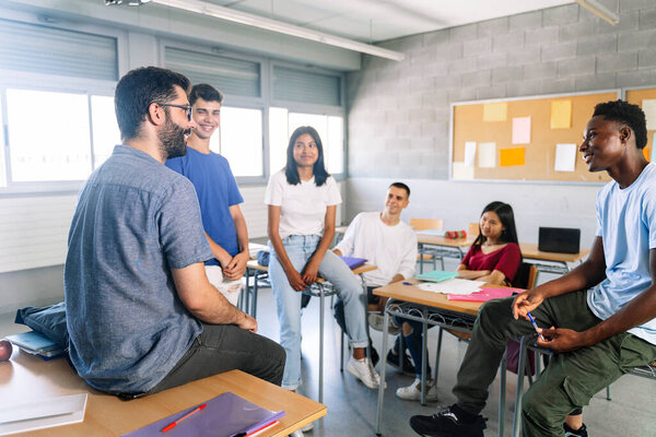 Teenager students listening and talking with friendly young male teacher - Group discussion in High School Education