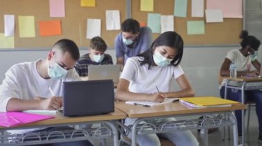 Teenager students learning at High school. Teacher wearing face masks helping students