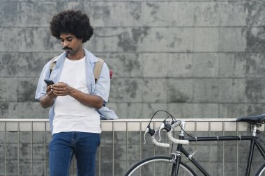 Young African American Man goes to work with bicycle using mobile cell phone in the city