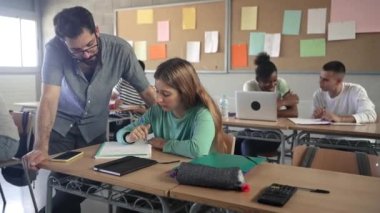 Young Professor helping female student in High School classroom. Friendly Teacher with beard explaining exercicse to blond girl