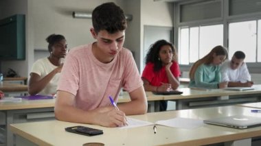 Teenager Boy Listening to a Professor Lecture and writing notes in a Classroom - Diverse Group of Multi Ethnic students learn at High School College