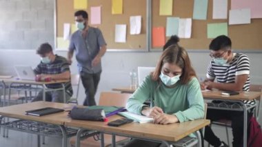 Teenager wearing face mask learning, writting assignment at School. Teacher helping students at College