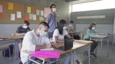 Teacher wearing face mask walks in the classroom explaining Lesson to class of Teenager students Learning at High School College