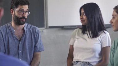 Friendly young male teacher talking to teenager students in a group discussion at High School 