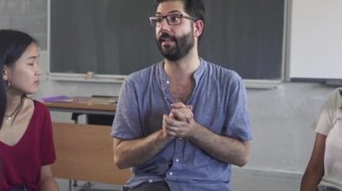 Confident young male mentor teacher talking to multiracial students - Teenagers sitting in a circle having a group discussion in High School classroom