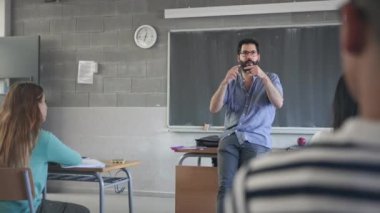Young passionate teacher with beard and eyeglasses explaining lesson to students in the school