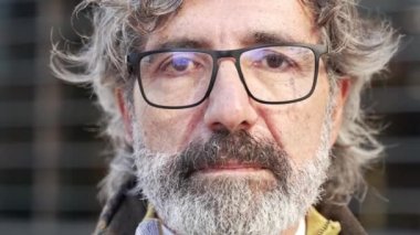 Sakallı ve gözlüklü yaşlı adam kameraya ciddi bir ifadeyle bakıyor. İnsan duygularının ve duygularının portresi
