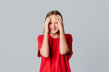 Şaşırtıcı bir şekilde şaşırmış, şaşırmış bir kız kameraya bakıyor. Başını tutuyor. Gördüklerine inanamıyor, gri arka planda dikilen sıradan kırmızı tişört giyiyor. Genç duygusal kadın.