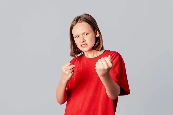 平和的なティーンの女の子は怒りと拳を示しています 歯を食いしばり 不正と暴力との戦い カジュアルな赤いTシャツに身を包んだ 見て決定しています 灰色の背景の上に立って — ストック写真
