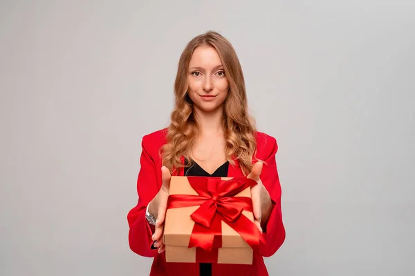 快乐的金发女人拿着红弓装饰的礼品盒 迷人的金发年轻女子穿着时髦的红色夹克 在灰色背景下显得孤立无援 元旦妇女生日假期的概念 — 图库照片