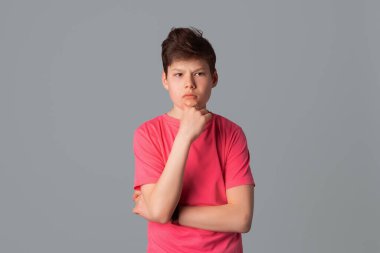 Sıradan pembe tişörtlü bir genç. Düşünürken, karar verirken, beyin fırtınası yaparken, gri arka planda düşünceli bir şekilde dikilirken gözlerini kaçırıyor.