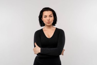 Beyaz bir arka planda kollarını kavuşturmuş kendine güvenen bir kadının portresi.