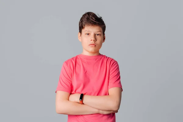 Pembe tişörtlü yakışıklı bir gencin portresi durgun bir şekilde duruyor kameraya bakıyor, kolları göğsünde, gri arka planda.