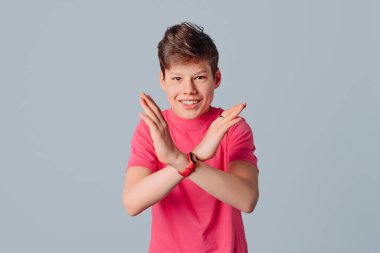 Sıradan pembe tişörtlü bir gencin portresi, x çapraz el hareketi yaparak anlaşmazlığı gösteriyor, gri arka planda duruyor.