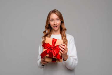 Güzel genç bir kadın el ele tutuşmuş ve kameraya şaşkın bir ifadeyle bakıyor, gri arka planda duruyor. Yeni yıl kadınlarının doğum günü konsepti