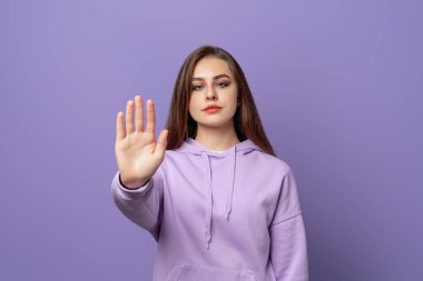 Hayır diyen hoşnutsuz öğrenci kız, reddedilme hareketi gösteriyor, olumsuz tavrını ifade ediyor, mor kapüşonlu giyiyor, mor arka planda duruyor. Uyarı kavramı, yasaklama