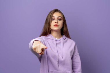 Genç esmer kadın seni işaret ediyor ve mor arka planda duran kızgın yüzlü kamera. Mor kapüşonlu genç duygusal kadın
