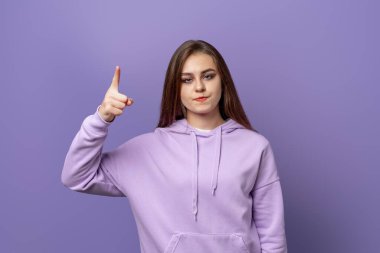 Öfkeli genç bir kadının portresi. Parmağını kaldırarak kameraya olumsuz bakıyor. Mor arka planda duruyor. Uyarı kavramı, yasaklama