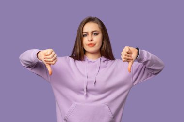 Senin için kötü haber. Tatmin olmamış genç esmer kadın, mor arka planda dikilirken teklif durumunu onaylamadığını gösteriyor. Negatif insani duygular, yüz duyguları