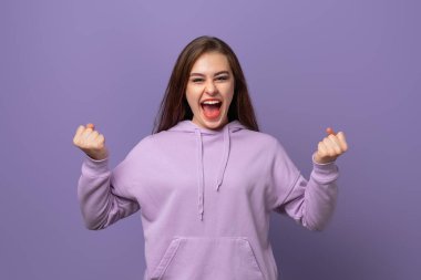 Mutlu genç bir kadın kollarını kaldırıp zafer işareti yapıyor, gülümsüyor ve başarı için bağırıyor. Kutlama konsepti