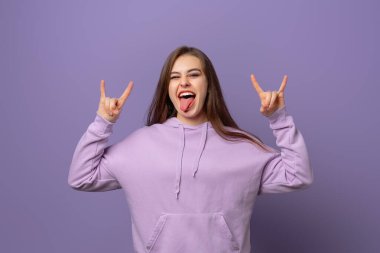 Vahşi ve özgür milenyumlar. Heyecanlı, esmer, mor kapüşonlu kız, harika öğrenci partisinde eğleniyor, dilini gösteriyor ve gülümsüyor, rock 'n roll hareketi yaparak heyecanı ifade ediyor.