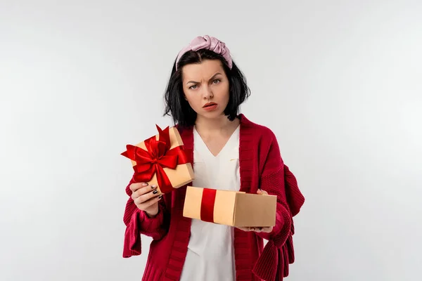 Portrait of a discouraged young woman opening a gift box decoration red ribbon, isolated over white background