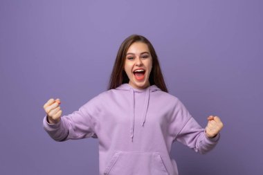 Mutlu galip. Mor arka planda dikilirken el kol hareketi yapan ve ağzını açık tutan mutlu genç esmer kadın. Kutlama konsepti