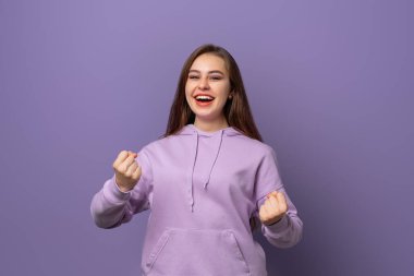 Mutlu galip. Mutlu genç esmer kadın mor arka planda durarak birinci sınıf jest yapıyor. Kutlama konsepti