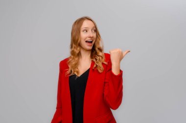 Hey şuraya bak. Gülümseyen, sarışın, sağı işaret eden, reklam veren, tanıtım yapan, gri arka planda kırmızı ceketli genç bir kadın.