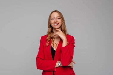 Kendine güvenen, sarışın, kırmızı ceketli güzel bir kadın. Çenesinin üstünde elini tutuyor ve kameraya samimi ve nazik bir şekilde gülümsüyor. İyi haberlere bakmaktan hoşlanıyor.