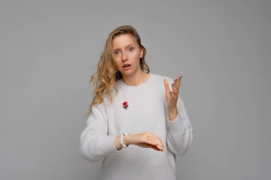 Young beautiful woman wearing cozy white sweater standing over gray background In hurry pointing to watch time, impatience, upset and angry for deadline delay