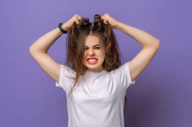 Woman is under huge mental pressure. Portrait of bothered devastated cute girl with long hair pulling out chestnut hair and shouting from regret, while standing over purple background